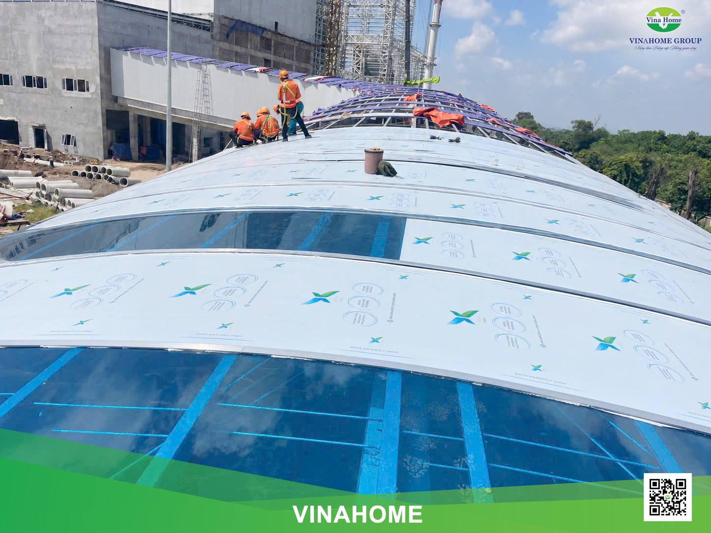 Thợ thi công đeo dây an toàn lắp tấm poly đặc xanh hồ trên mái vòm